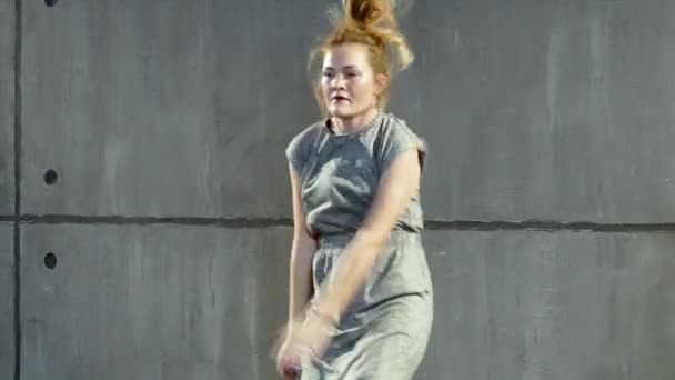 Jonge blonde vrouw voert in grijs kleren in de buurt van de muur — Stockvideo