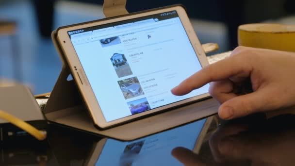 Hombre explorando eBay sitio en busca de coches Tesla de segunda mano utilizando tableta PC en la cafetería . — Vídeos de Stock