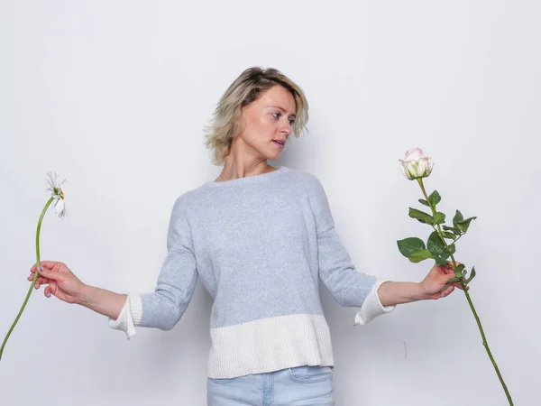 Porträtt av ung blond vacker kvinna med makeup i naturlig casual klänning välja mellan två blommor — Stockfoto