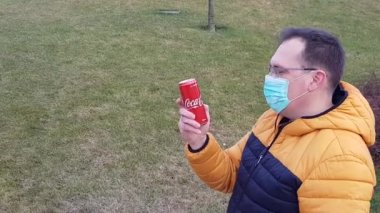 Sick man in medical mask drinks coke outdoors