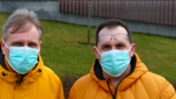 Couple of men in medical masks cautiously approach and look into the lens — Stock Video