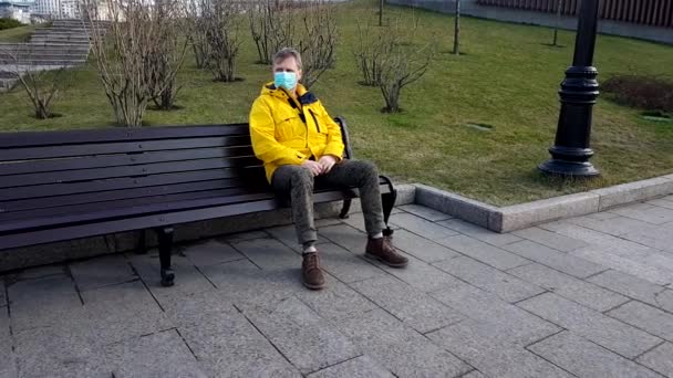 Sick man take on medical mask sitting on a park bench — Stock video