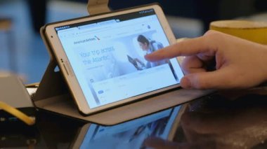 Adam kafedeki tablet bilgisayarla American Airlines şirketinin sitesini ziyaret ediyor.