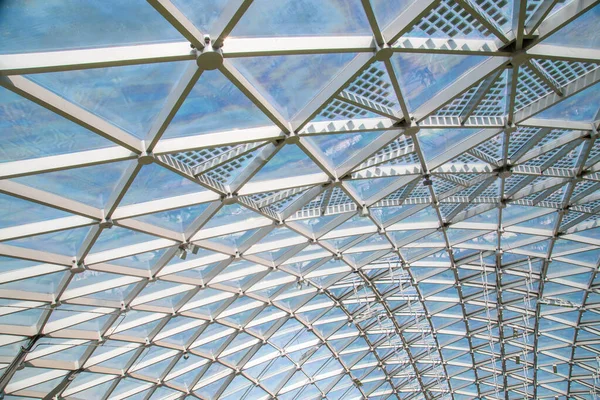 Abstract high-tech architecture background photo, internal structure of glass roof arch with lockable windows sections. Transparent glass roof of a modern building with blue sky and clouds — ストック写真