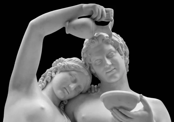 La escultura de mármol de la joven pareja romana. Primer plano de una escultura de un hombre y mujeres mirando amorosamente a los ojos de los demás. Joven mujer romana desnuda y hombre en unidad aislado sobre fondo negro —  Fotos de Stock