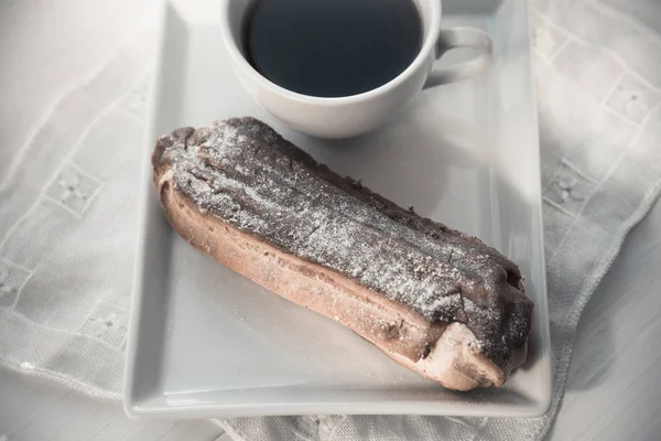 Eclair de chocolate no prato e xícara de café — Fotografia de Stock