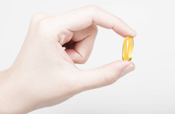 Female hand with clear shiny yellow Vitamin E capsule on white background