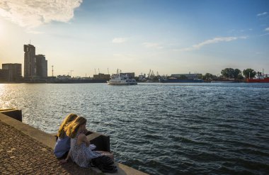 GDYNIA, POMERANIAN VOIVODESHIP / POLAND - JULY 27, 2018: Two girls are sitting on the pier at sunset. Gdynia, Baltic Sea