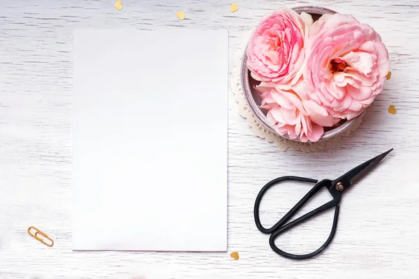 Pembe güller ve beyaz masada boş kağıt — Stok fotoğraf