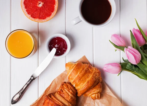Ontbijt met croissants en koffie en roze tulpen op de whit — Stockfoto