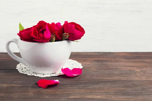 Kytice červených růží v bílé cup na dřevěný stůl — Stock fotografie