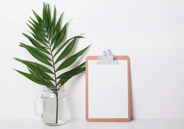 Clipboard with empty paper and tropic leaf in the jar. — Stock Photo, Image