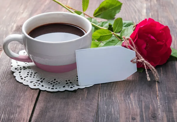 Fincan kahve, kırmızı gül ve boş bir hediye etiket ahşap tablo — Stok fotoğraf