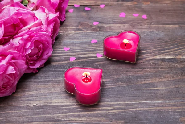 Roze rozen en twee hart vormige kaarsen op de houten achtergrond — Stockfoto