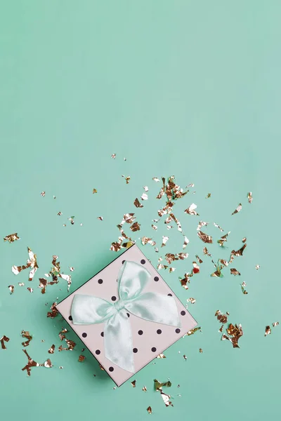 Polka dot giftbox versierd met strik op turquoise achtergrond met gouden glanzende glitter confetti — Stockfoto