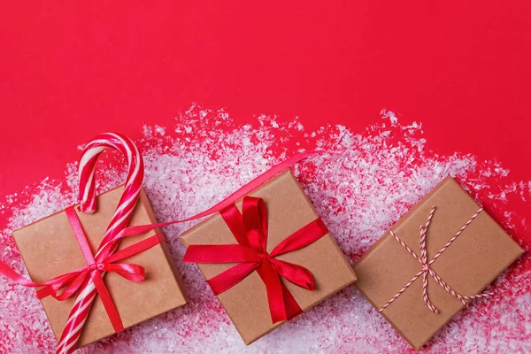 Christmas presents in boxes on red table with snow. — Stock Photo, Image