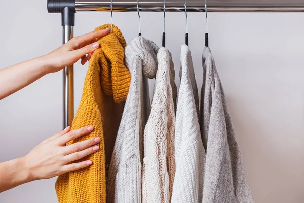 Mani delle donne che scelgono maglione a maglia gialla tra gli altri su appendiabiti — Foto Stock
