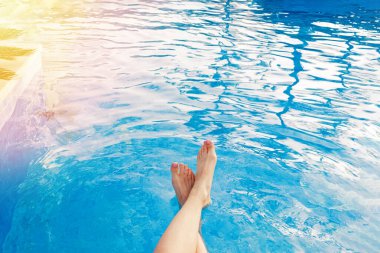 Kadın ayakları yüzme havuzunda suya dokunuyor.