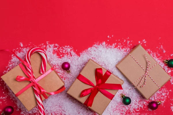 Kerstcadeau dozen en kleine ballen op rode achtergrond met decoratieve sneeuw — Stockfoto