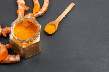 Cam kavanozda zerdeçal tozu ve siyah arka planda kaşık..