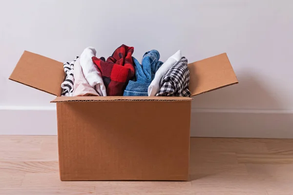 Cardboard box full of clothes standing on the floor.