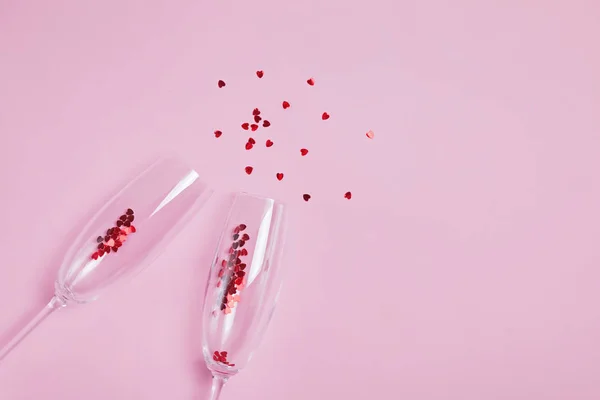 Zwei klirrende Sektgläser mit rotem Herzkonfetti auf rosa Hintergrund. — Stockfoto