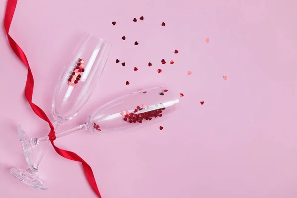 Sektgläser mit rotem herzförmigem Konfetti und Band auf rosa Hintergrund. — Stockfoto