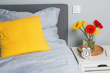 Modern yatak odasının içinde parlak dekoratif yastıklar ve parlak çiçekler var..