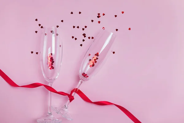 Two champagne glasses, red ribbon and heart shaped confetti splashes. — Stock Photo, Image