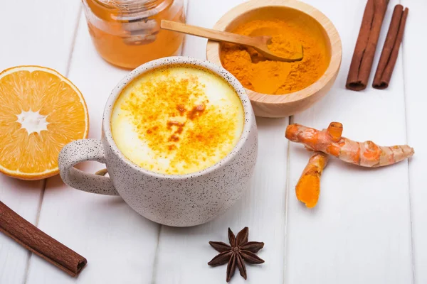 Detox turmeric tea golden milk and ingredients on white wooden table
