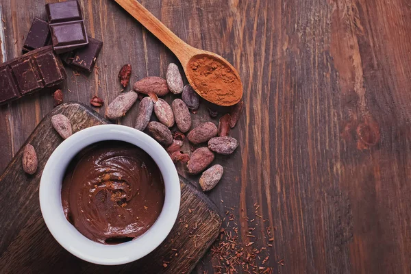 Crema de chocolate, granos de cacao y polvo y trozos de chocolate en la mesa de madera —  Fotos de Stock