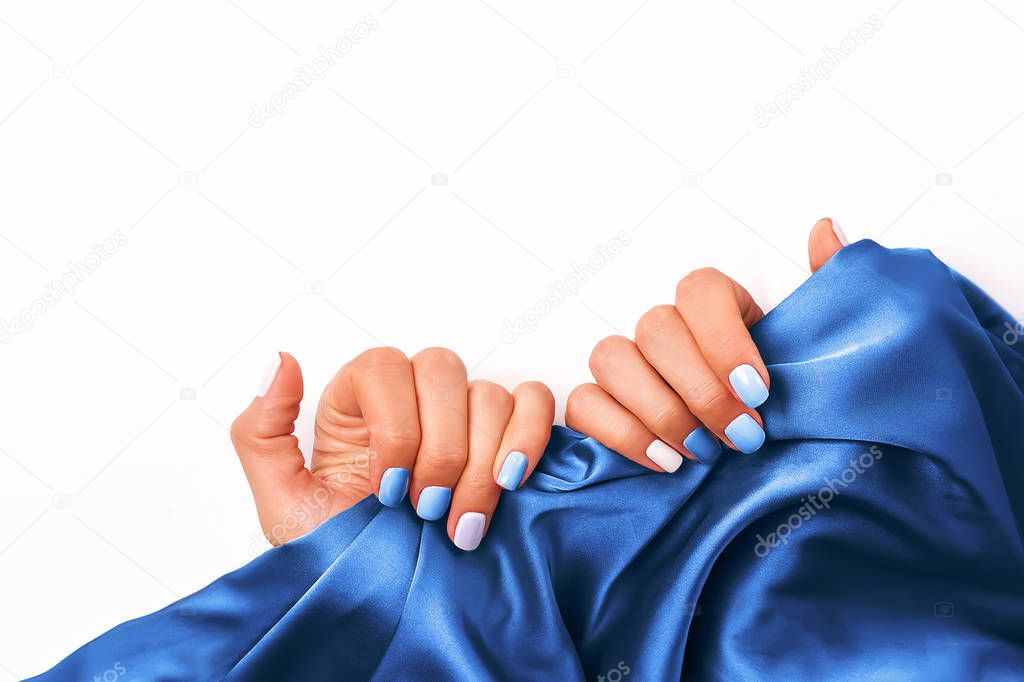 Womans hands close-up with beautiful salon manicure of different colors holding a blue silk
