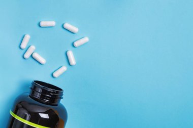 Açık mavi arkaplanda izole edilmiş kavanoz ve haplar, üst görünüm.