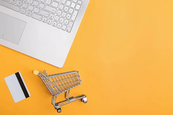 Laptop, credit card and small shopping trolley on yellow background — ストック写真