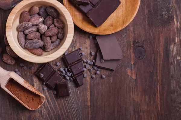 Fagioli di cacao e pezzi di barrette di cioccolato e polvere su sfondo di legno — Foto Stock