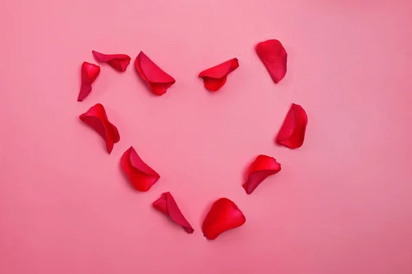 Corazón dispuesto a partir de pétalos de rosa roja aislados sobre fondo rosa — Foto de Stock