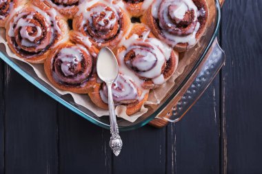 Cinnamon rolls with white icing on top standing on black wooden table clipart