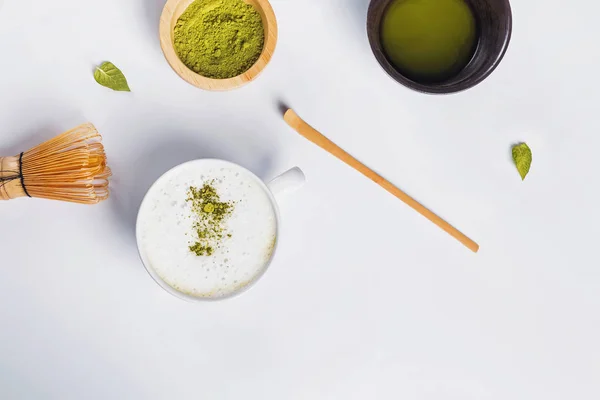 Matcha Latte in einer Tasse, grünes Pulver in einer Holzschale und Werkzeuge für die Teezubereitung — Stockfoto