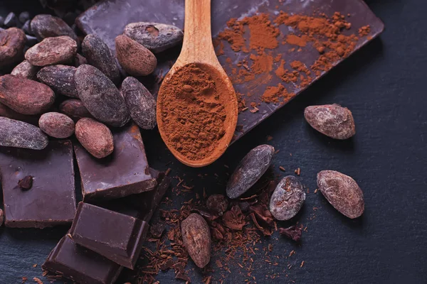 Chocolate natural y cacao en polvo en una cuchara de madera sobre bacgkround de piedra negra —  Fotos de Stock