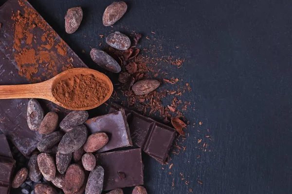 Chocolate natural y cacao en polvo en una cuchara de madera sobre bacgkround de piedra negra —  Fotos de Stock