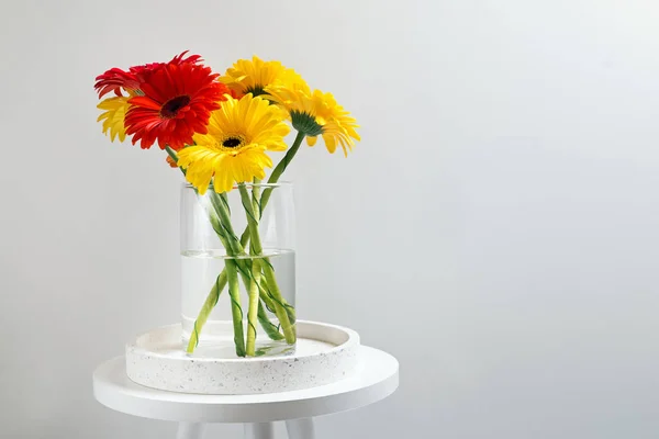 Colorful bunch of gerbera flowers in a glass vase standing near the white wall. — Stock Photo, Image