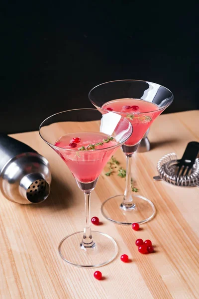 Dos vasos de martini llenos de color rojo cóctel de arándanos y herramientas de barmen en la mesa de madera . — Foto de Stock