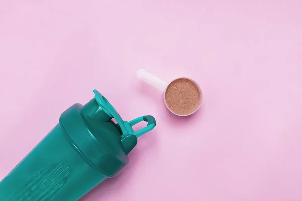 Protein shaker and scoopon chocolate porein on pink background,