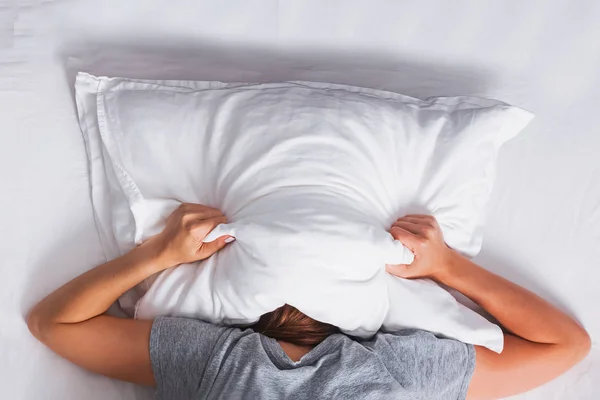 Жінка лежить на ліжку і покриває голову подушкою . — стокове фото