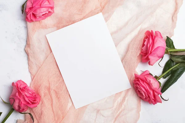 Top view of blank paper card lying on the pastel color cloth on the table with pink roses. — Stok fotoğraf