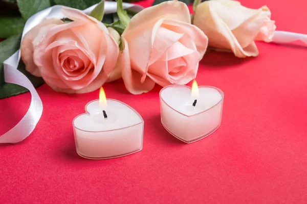 Twee hartvormige kaarsen en zachte pastelkleurige rozen op rode achtergrond close-up. — Stockfoto