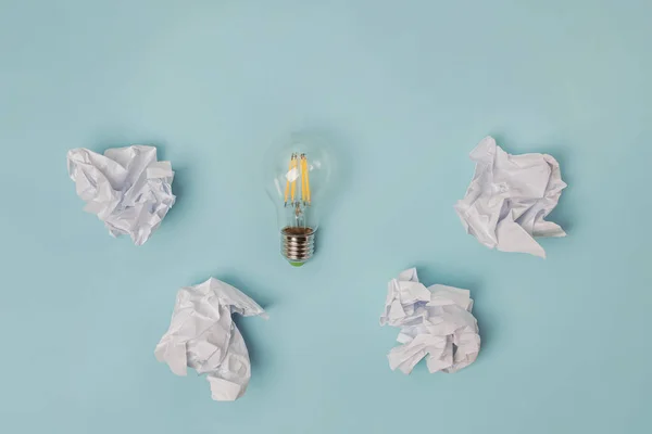 Crumpled office paper and light bulb lying on the table. Royalty Free Stock Photos