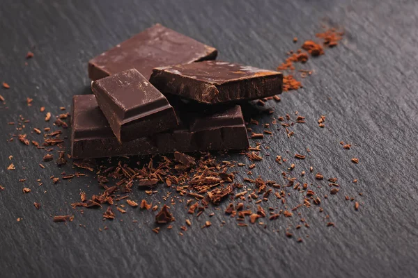 Pedazos de barra de chocolate sobre el fondo de piedra negra — Foto de Stock