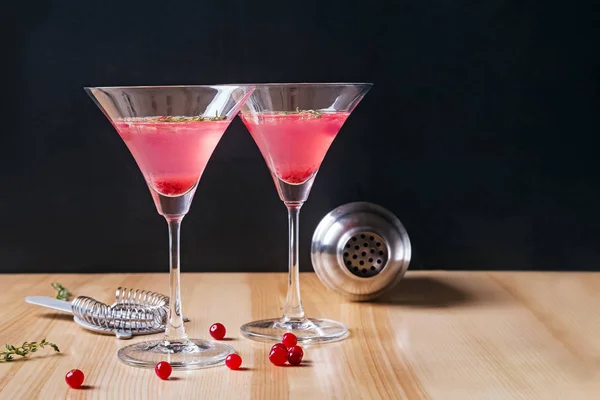 Dos vasos de martini llenos de color rojo cóctel de arándanos y herramientas de barmen en la mesa de madera — Foto de Stock