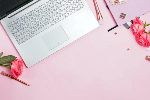 Conceito de espaço de trabalho feminino. Vista superior de laptop, papelaria cor dourada e rosas na mesa rosa . — Fotografia de Stock